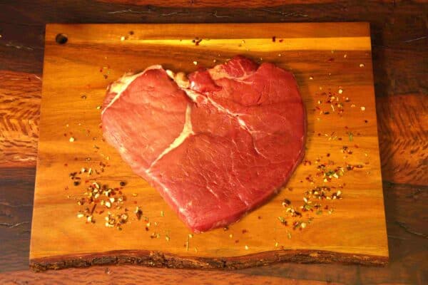 Carne natural madurada en forma de corazón en tabla de madera con especias.