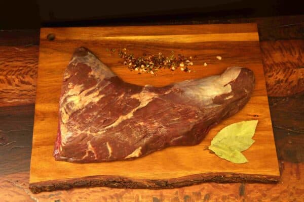 Carne natural madurada Delirio Res en tabla de madera con especias y hoja de laurel.