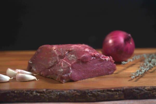 Carne natural madurada Delirio Res con ajo, cebolla y especias en tabla de madera.