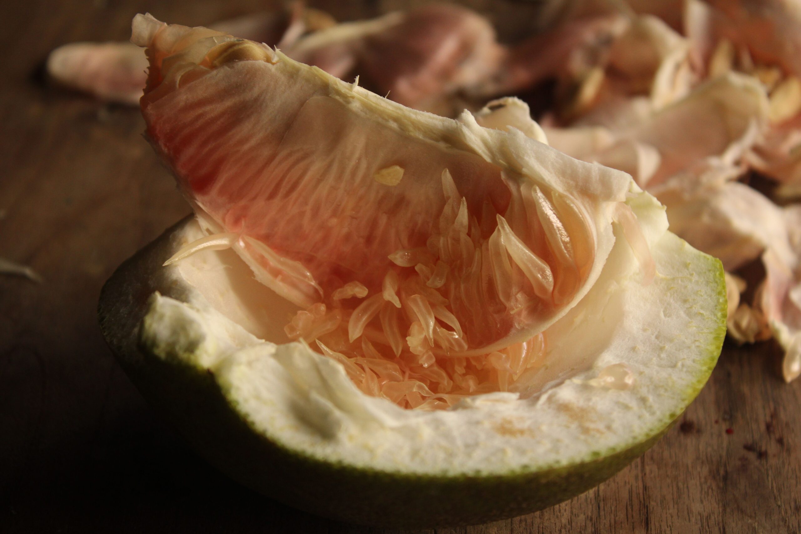 Vista detallada de un pomelo pelado que deja ver su jugoso interior, reposando sobre una mesa de madera.